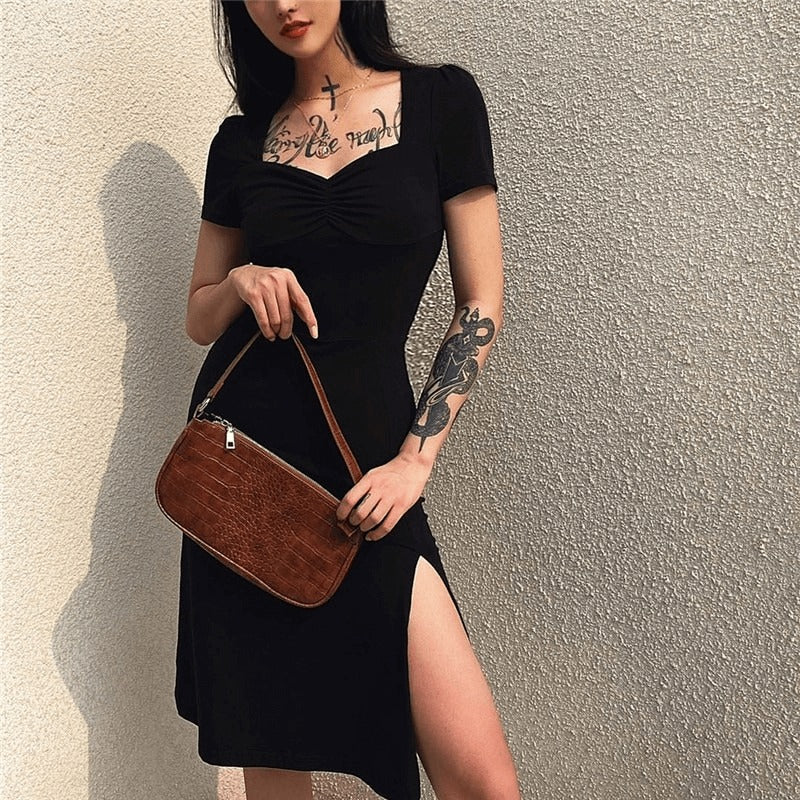 Fashionable woman in a square neck black dress with a side split, showcasing a gothic style and elegance.