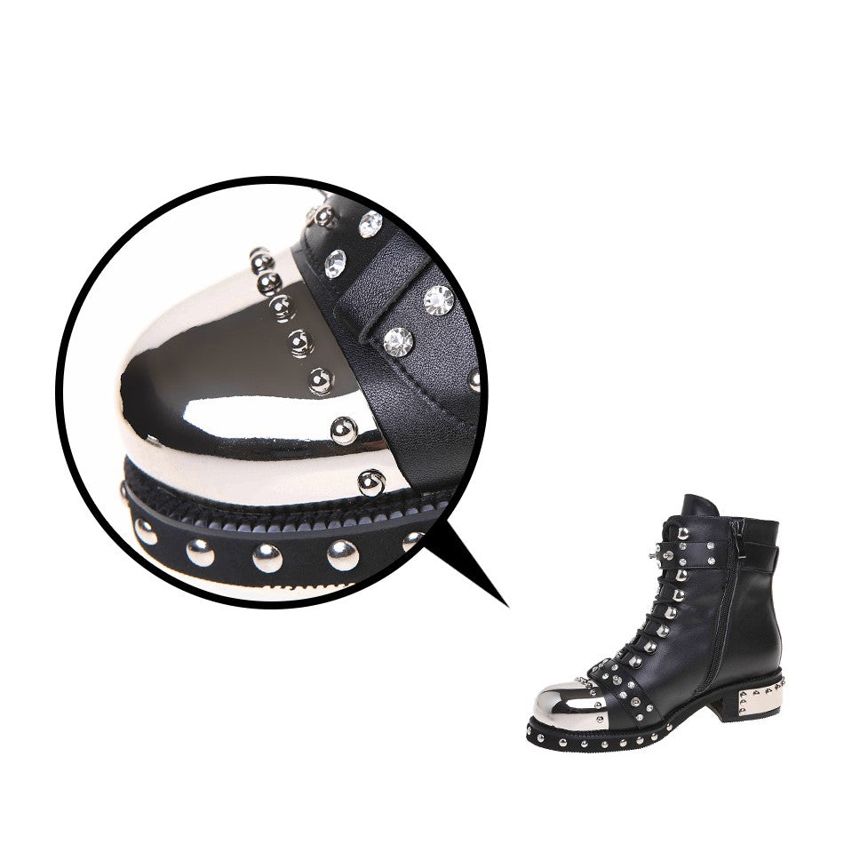Close-up of women's punk rock boots featuring shiny metal toe cap and decorative rivets on a stylish black leather design.