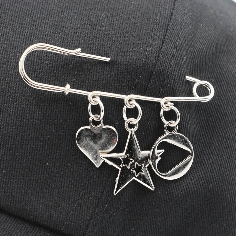 Silver safety pin with heart, star, and peace charms on a black baseball cap.