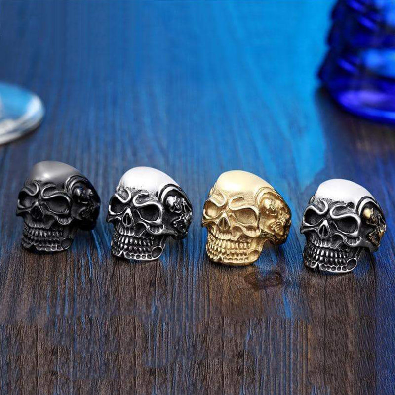 Trendy big triple skull rings in black, silver, gold, and white on a wooden table, perfect for rock style fashion.