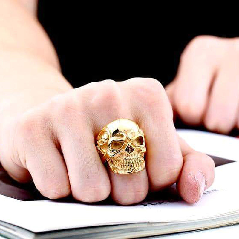 Big gold skull ring on a hand, showcasing alternative fashion biker jewelry style.
