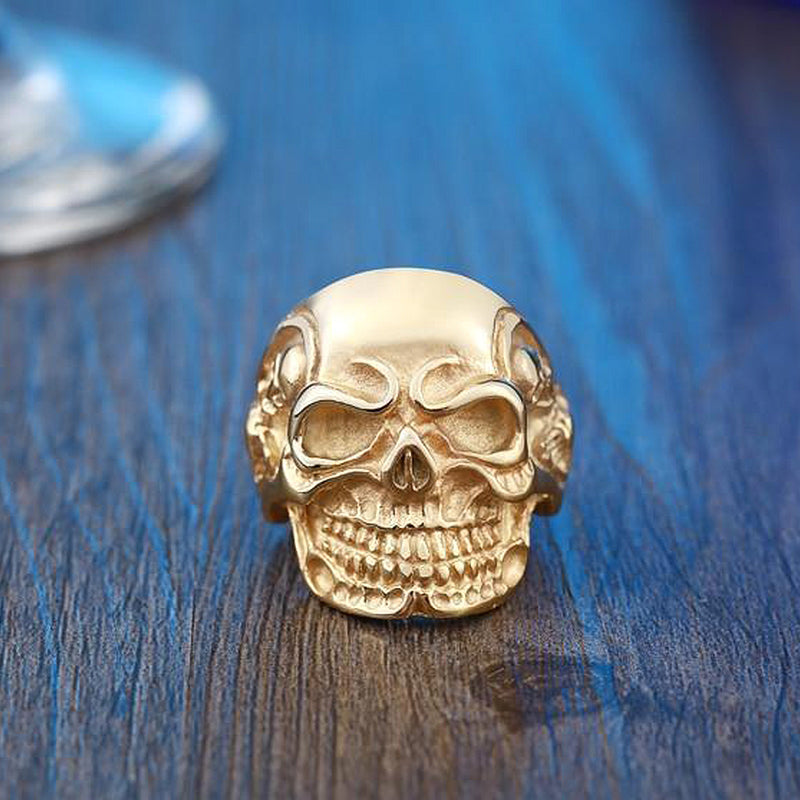 Big triple skull ring in gold, showcasing rock style biker jewelry on a wooden table.