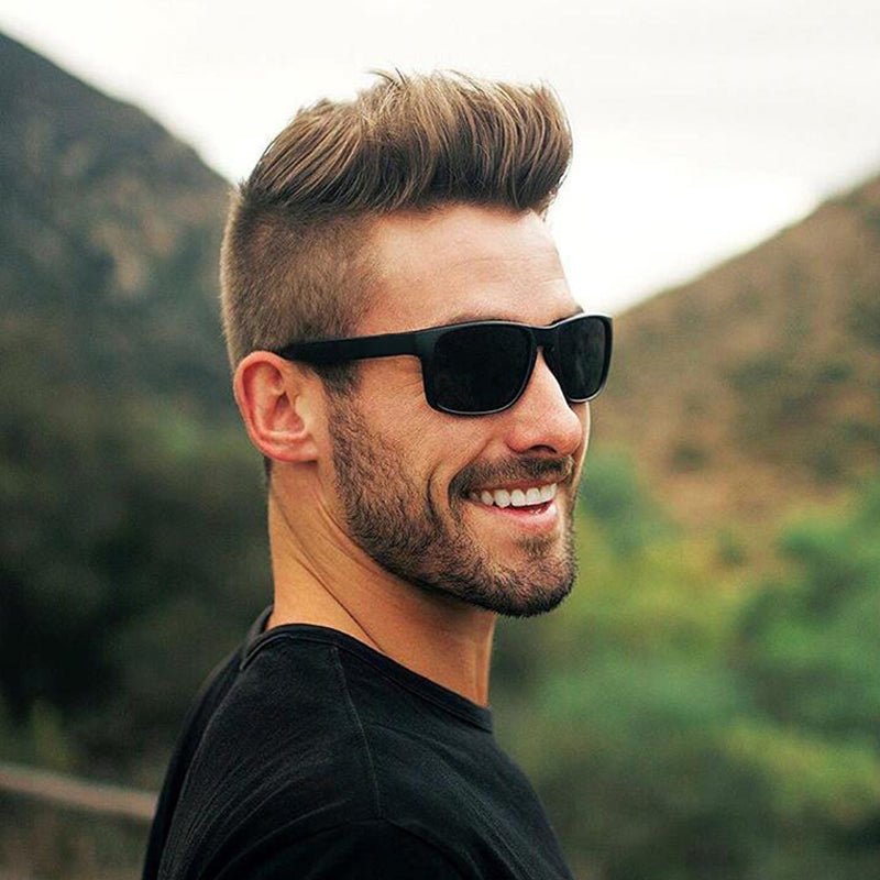 Stylish man wearing black square polarized sunglasses in a scenic outdoor setting.