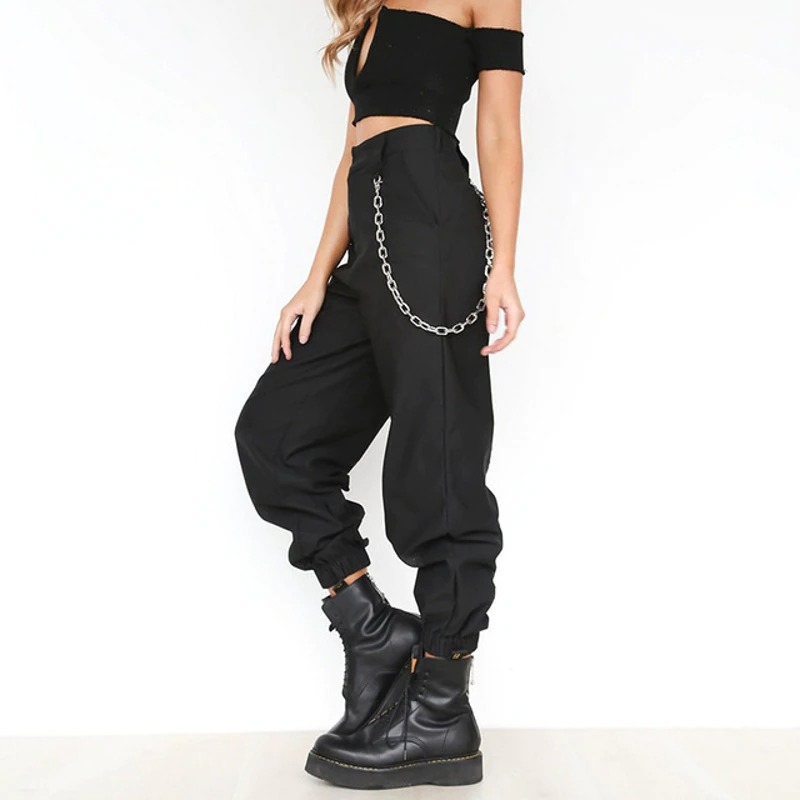 Alternative fashion women's high-waist black cargo pants with chain detail, styled with a crop top and boots.