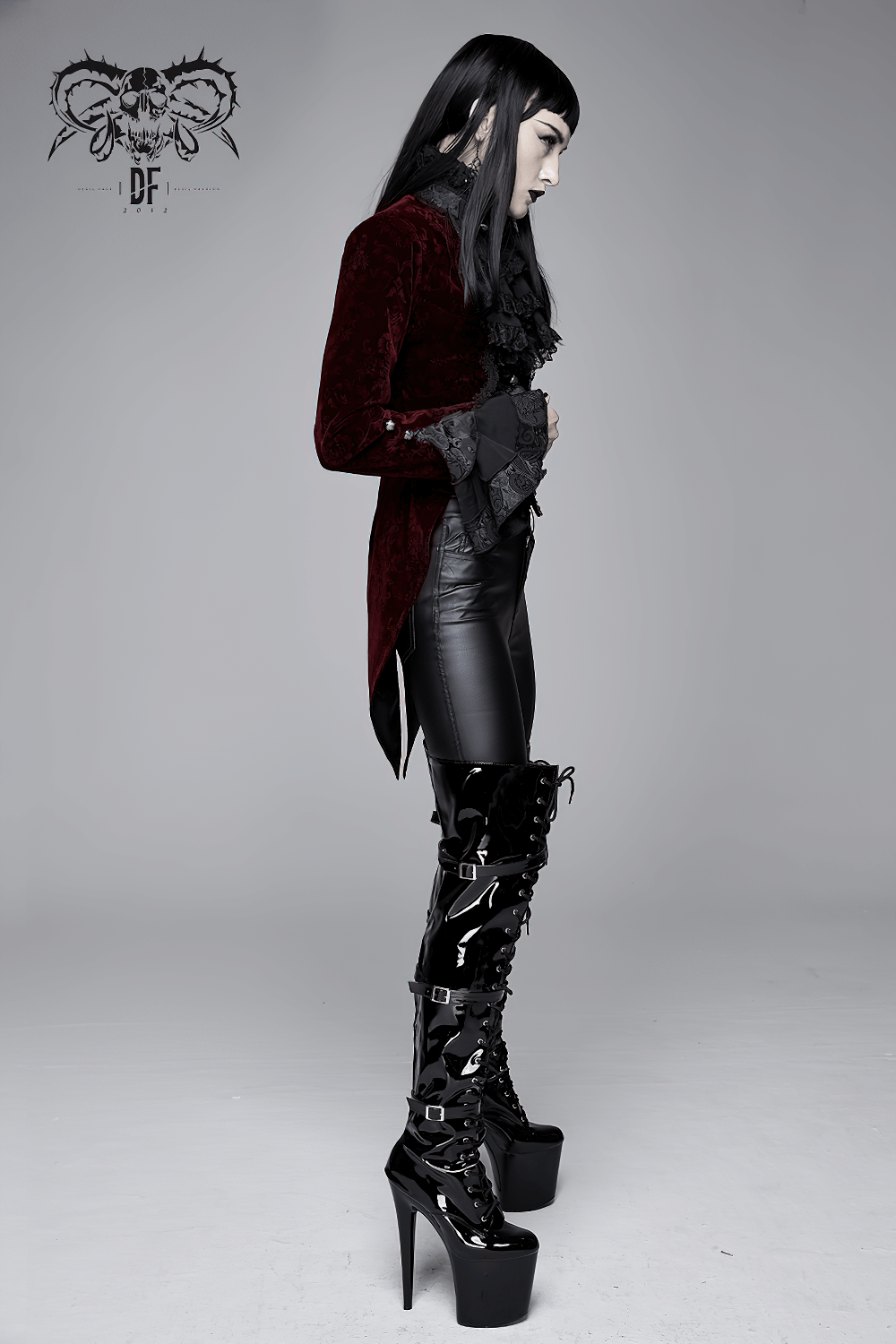 Model in a wine red Gothic velvet jacket, paired with black leather pants and shiny high-heeled boots, showcasing retro style.