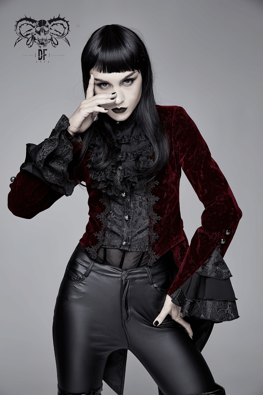 Elegant woman in a wine red gothic jacket with ruffles, showcasing a stylish retro look against a plain background.