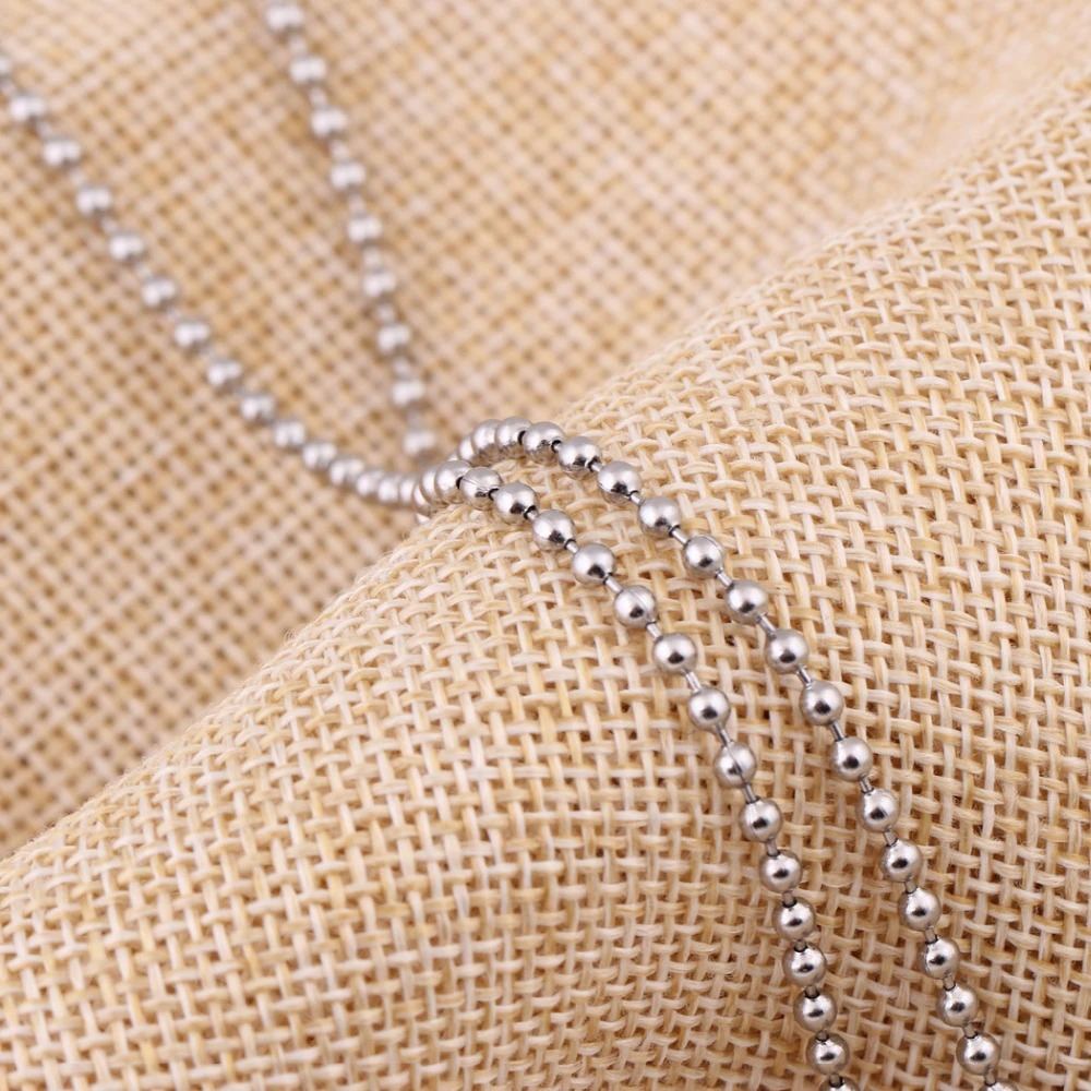 Close-up of a stainless steel necklace chain on textured fabric, showcasing its elegant bead design.