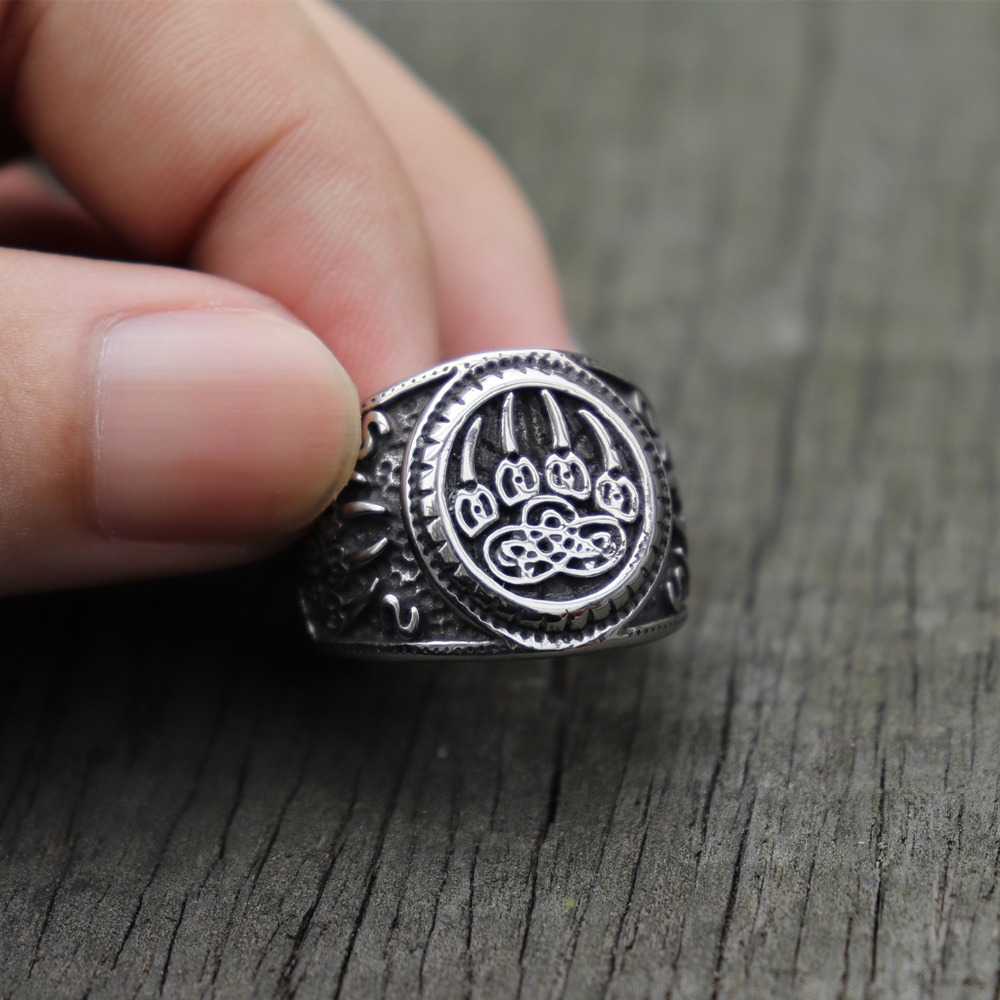 Hand holding a Bear Paw stainless steel ring with intricate Celtic knot design on a rustic wooden surface.