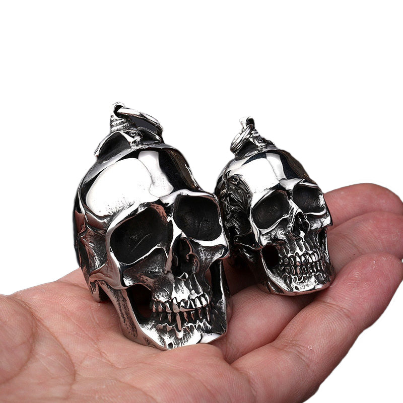 Big and small stainless steel skull pendants in hand, perfect for creepy accessory lovers.