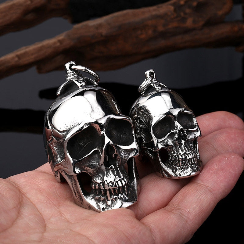 Big and small stainless steel skull pendants in hand, perfect for creepy accessory lovers.