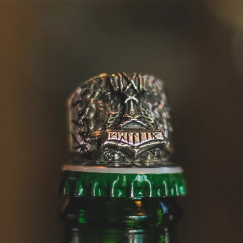 Biker ring with rune design placed on a green bottle cap, showcasing stylish men's jewelry.