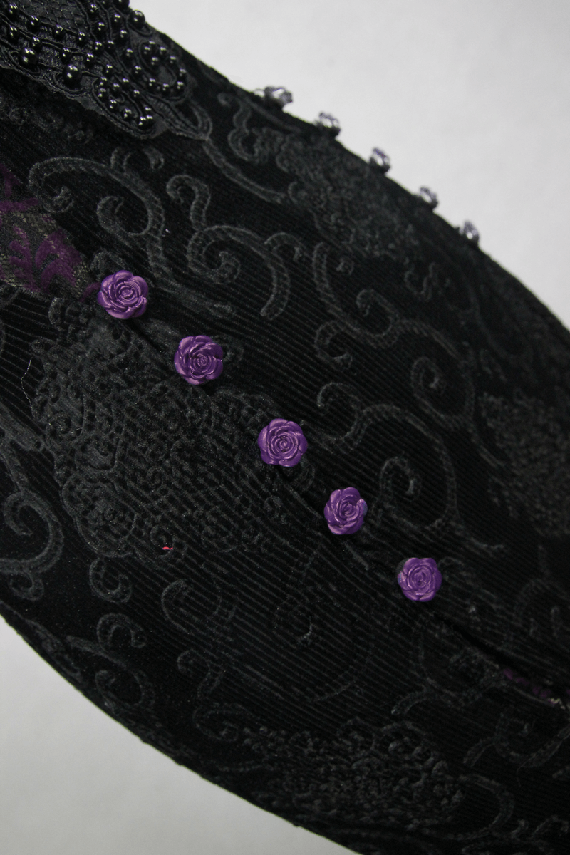 Close-up of a black lace fabric featuring purple decorative roses and intricate detailing, perfect for gothic fashion.