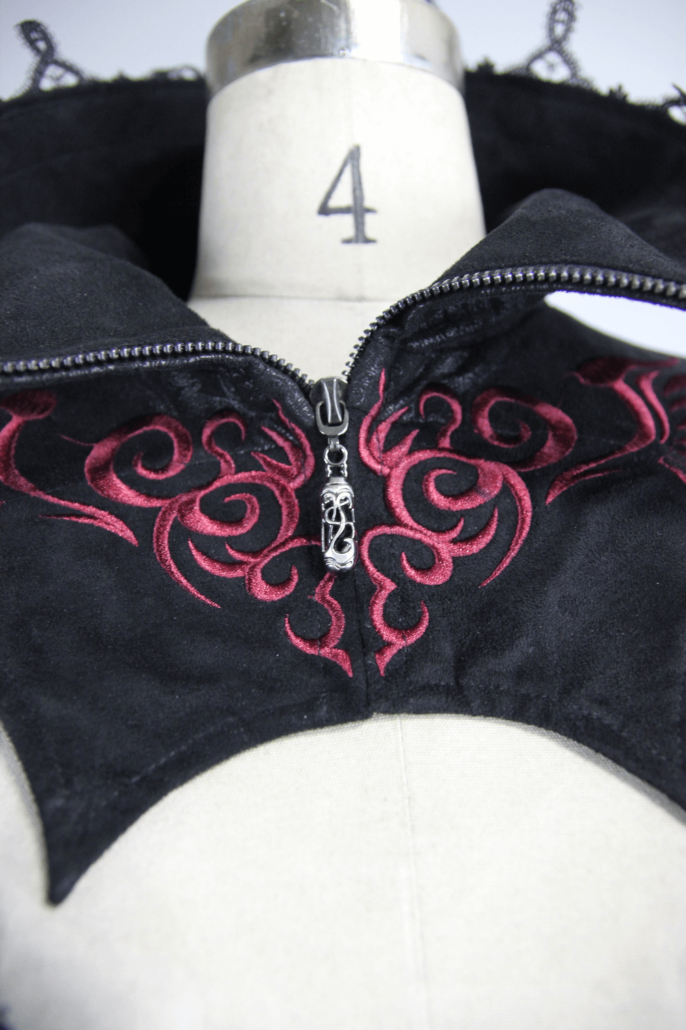Close-up of black and red embossed Gothic coat zippers and decorative design, showcasing intricate lacing and stand collar.