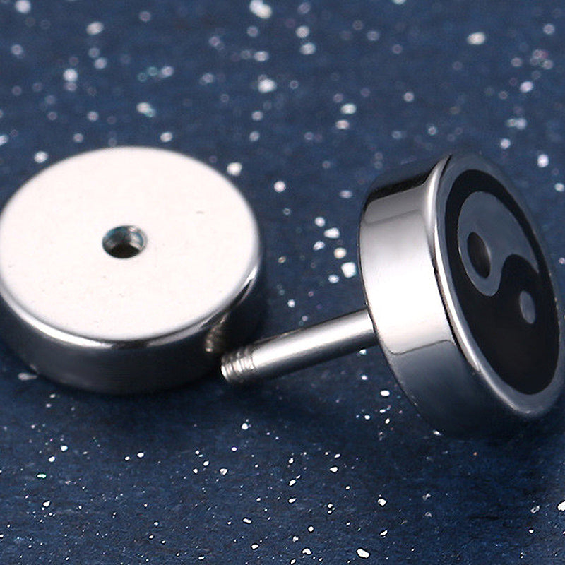 Black and white yin-yang stud earrings on a dark sparkly background, perfect unisex accessories for any outfit.