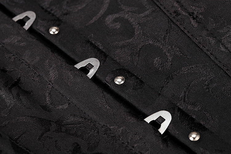 Close-up of black gothic corset detailing with belly closure and metallic fasteners on a textured fabric.