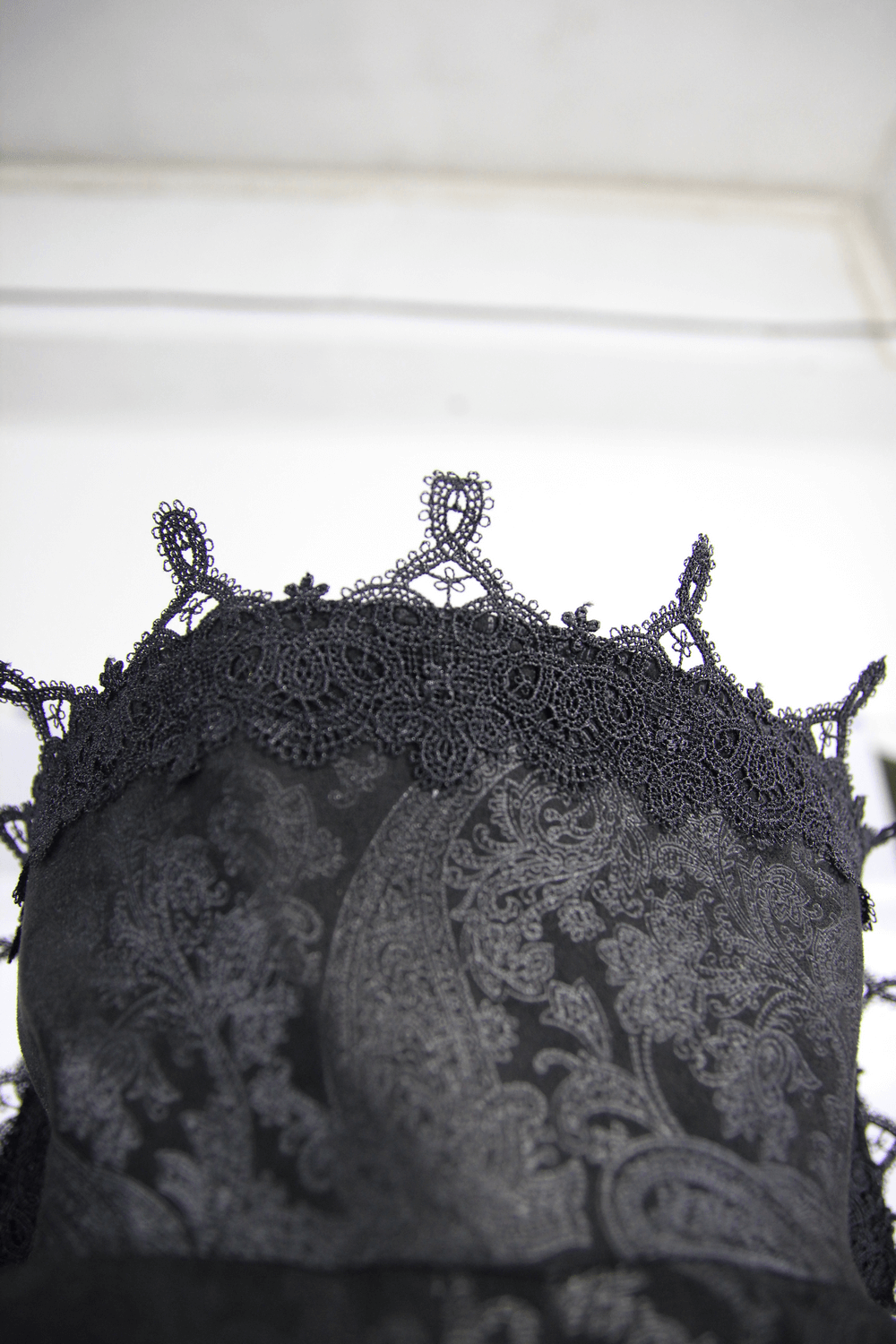 Close-up of the intricate lace detailing on a black embossed Gothic long coat with a high collar.