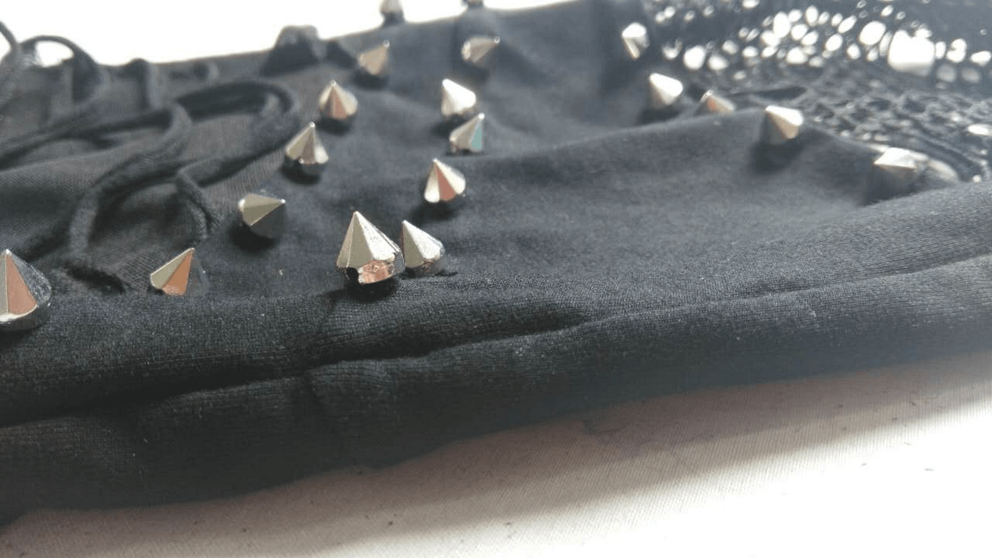 Close-up of black flared pants featuring edgy silver spikes and lace inserts for gothic fashion style.