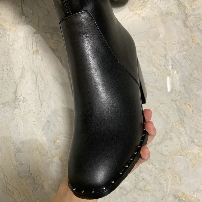Close-up of black genuine leather women's boot with round toe against a textured background.