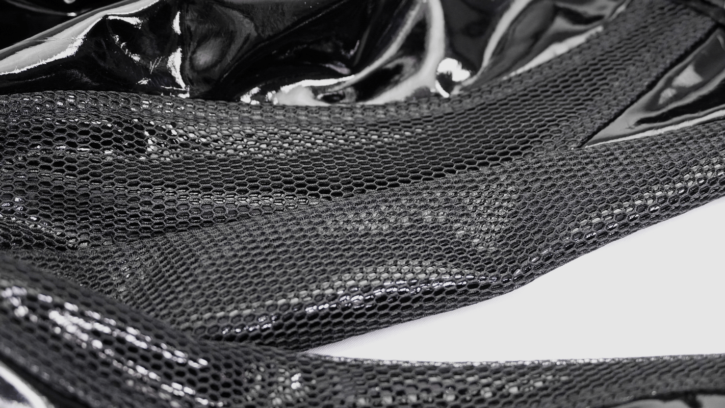 Close-up of black PU leather and mesh detail on gothic punk style men's pants.