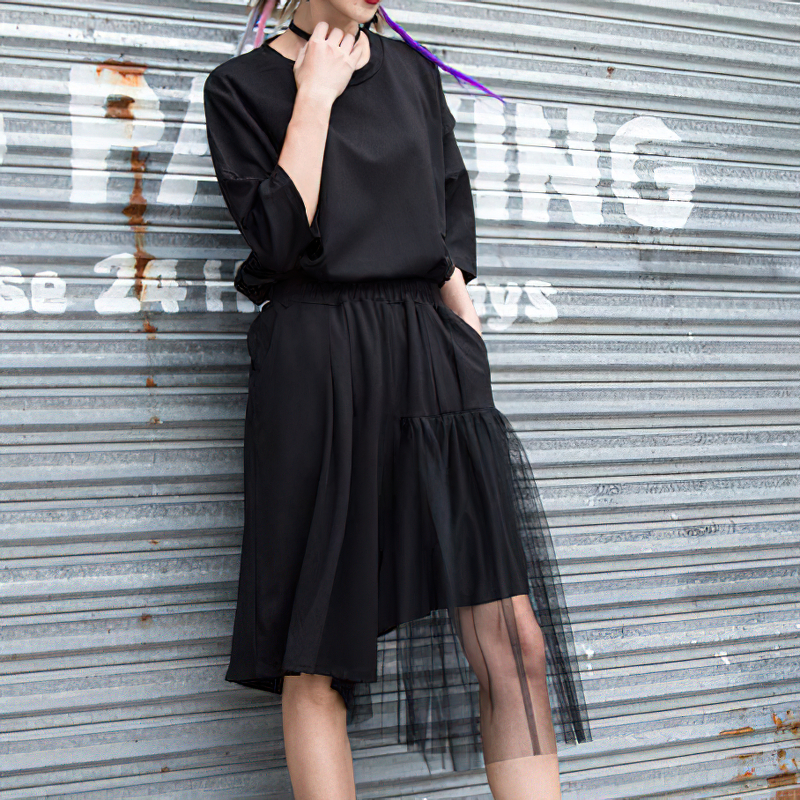 Model wearing black irregular half length trousers with high elastic waist and mesh layer, perfect for alternative fashion.