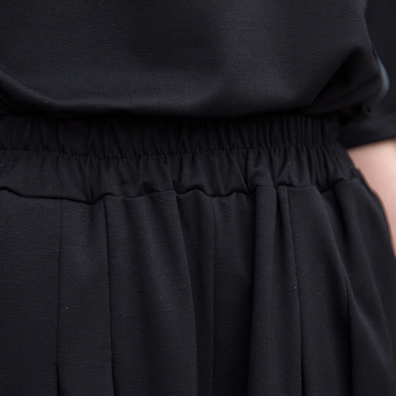 Close-up of high elastic waist of black irregular half length trousers, showcasing loose fit and stylish design.