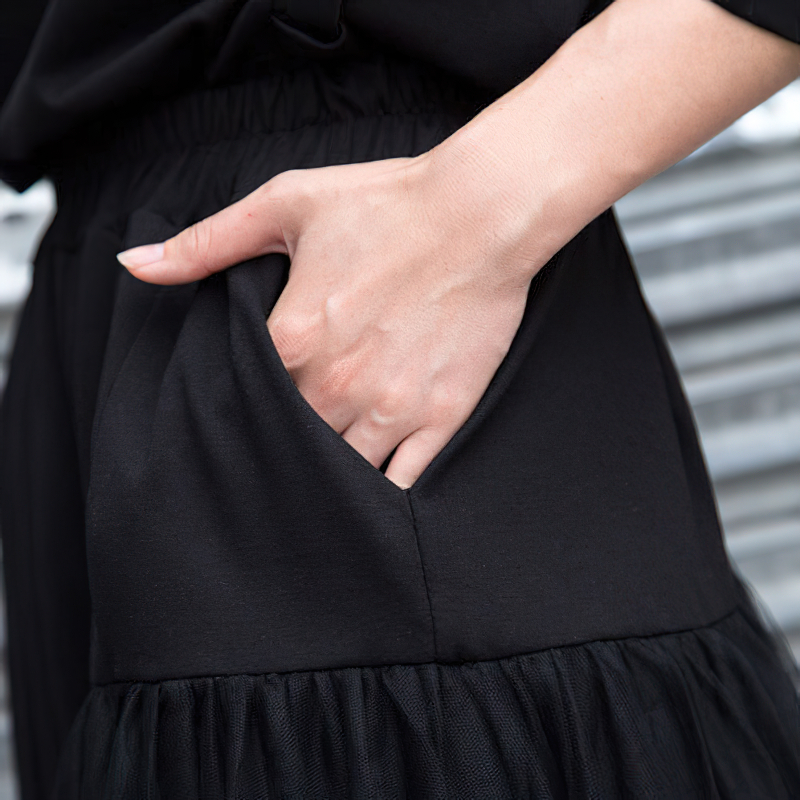 Close-up of hand in pocket of black asymmetrical trousers with elastic waist, perfect for alternative fashion.