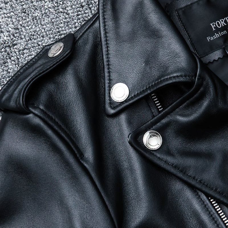 Close-up of a stylish black men's genuine leather jacket featuring silver snaps and a smooth finish on a textured background.