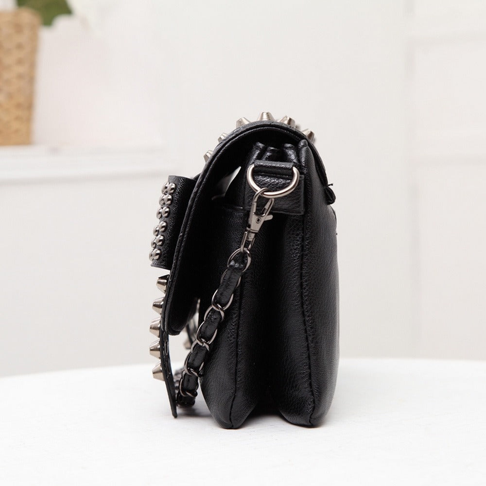 Side view of a black messenger bag with skulls and studs, showcasing the chain strap and rock style details.