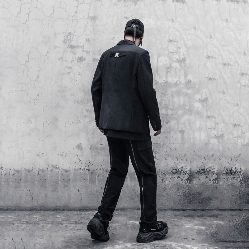 Stylish man wearing a black outfit with cargo pants and a blazer, featuring original design elements, walking away.