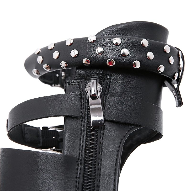 Close-up of black women's flat sandals featuring ankle strap, metal rivets, and zipper for stylish summer wear.