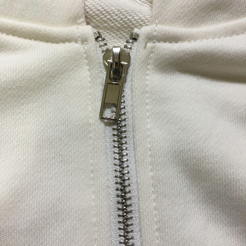 Close-up of a white hoodie zipper showcasing metallic detailing and smooth fabric finishing.