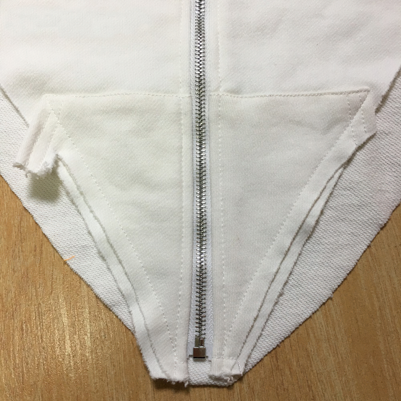 Close-up of a white hoodie zipper with unique cut details, perfect for alternative fashion and vintage goth styles.