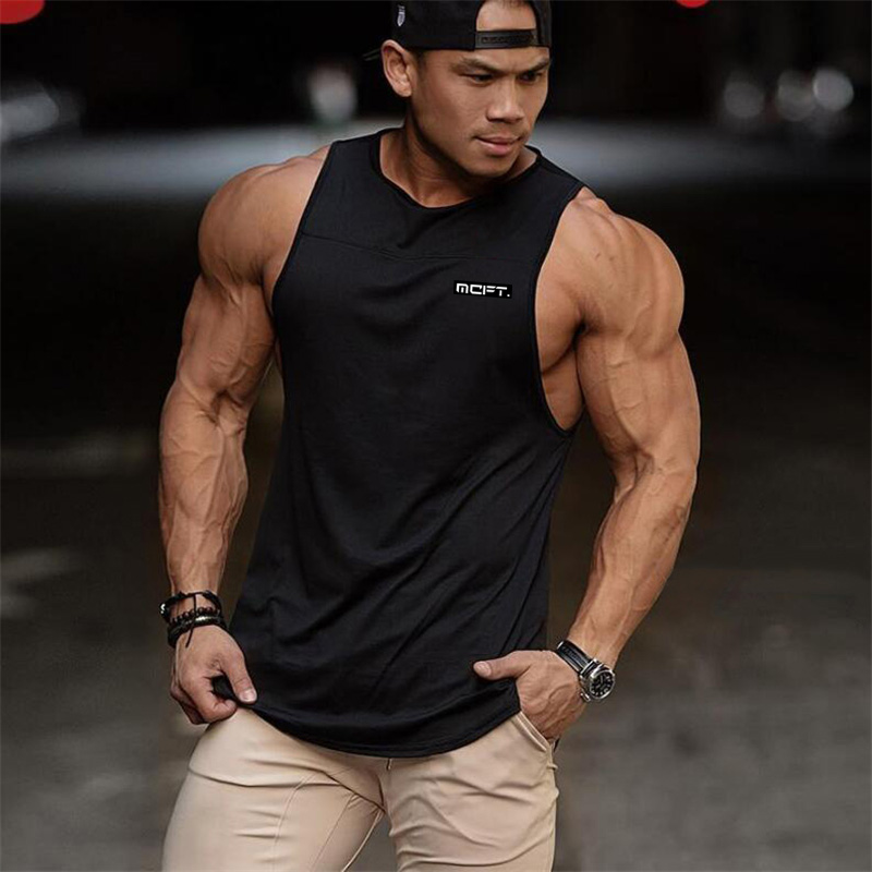 Muscular man wearing a black bodybuilding tank top, showcasing athletic style and cotton comfort in an urban setting.