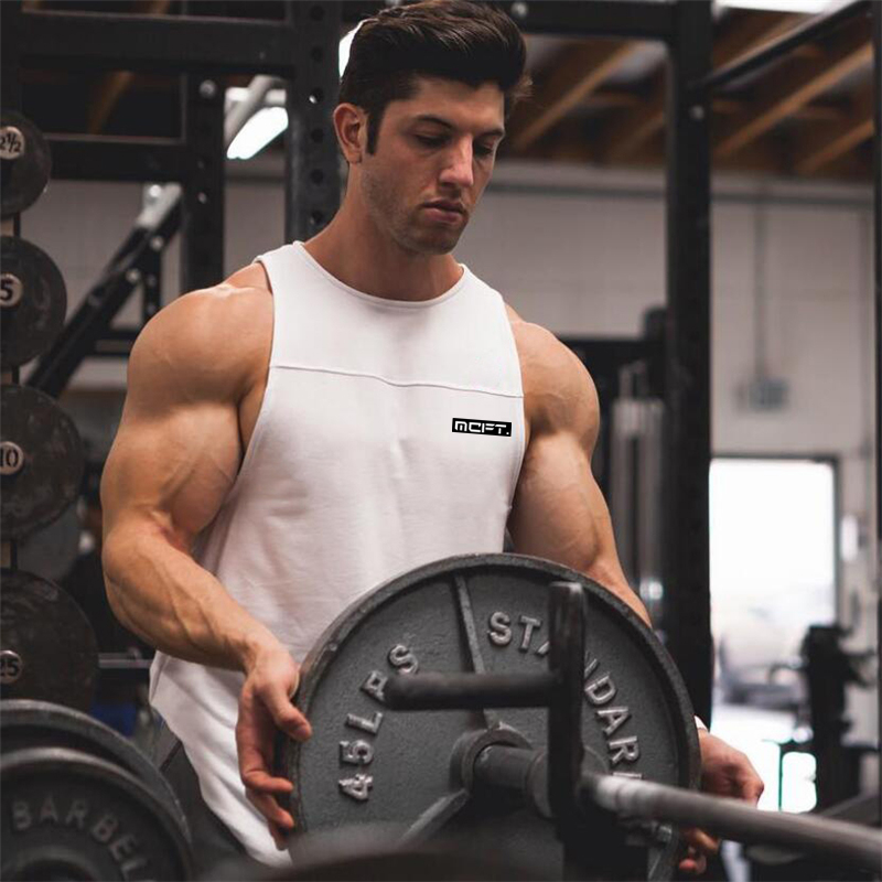 Muscular man lifting weights in a white bodybuilding tank top, showcasing sporty style at the gym.