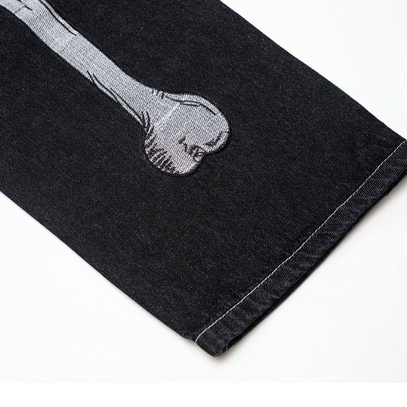 Close-up of bone print on black men's jeans, showcasing unique alternative style and fashion details.
