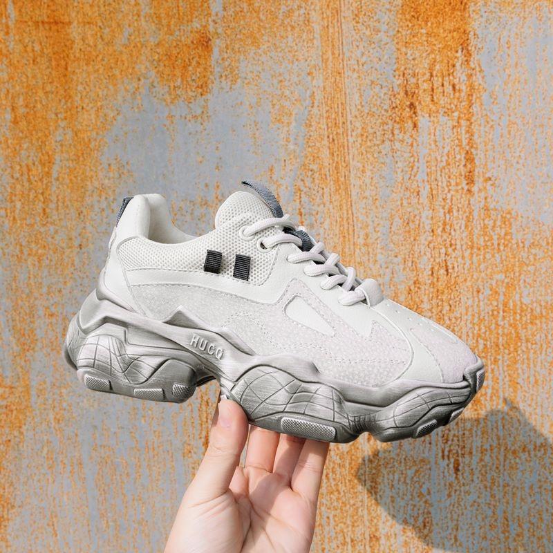 Hand holding stylish breathable women's sneakers in white and gray on a textured background. Perfect casual footwear!