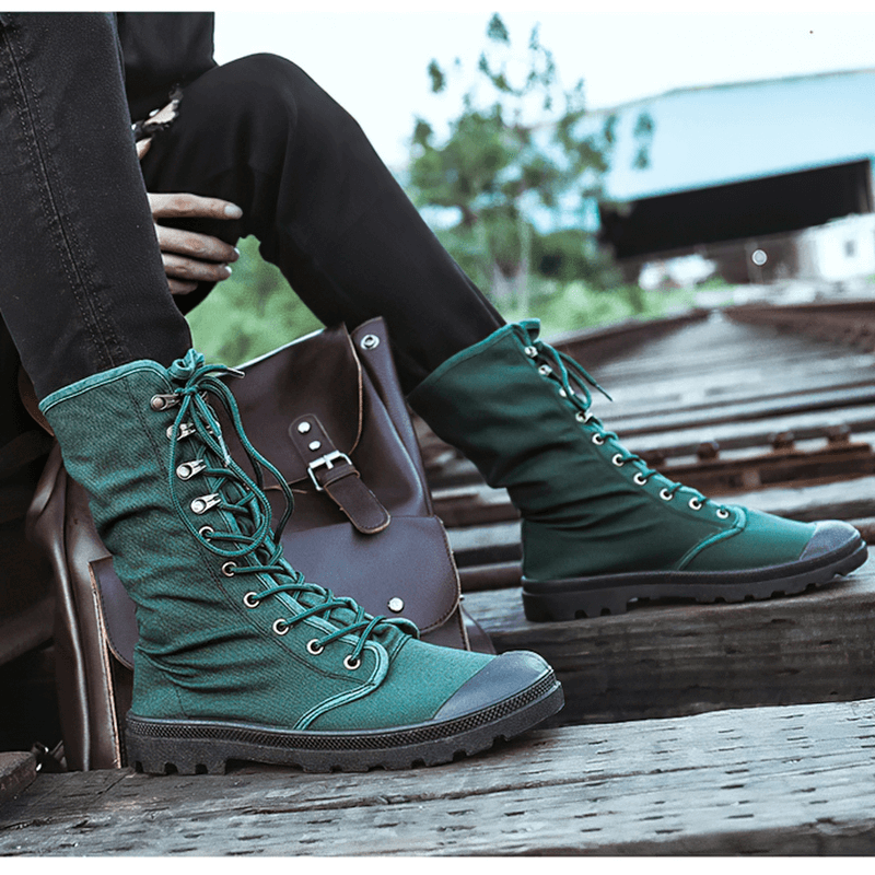 Men's mid-calf lace-up canvas boots in green, styled casually on a pathway with a shoulder bag.