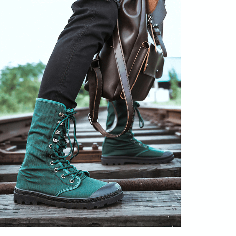 Stylish green canvas lace-up boots with a rugged sole, paired with casual black pants and a brown bag, on train tracks.