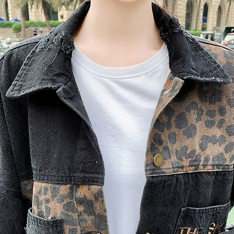 Close-up of casual women's denim jacket with leopard print patches, featuring frayed collar and a white t-shirt underneath.