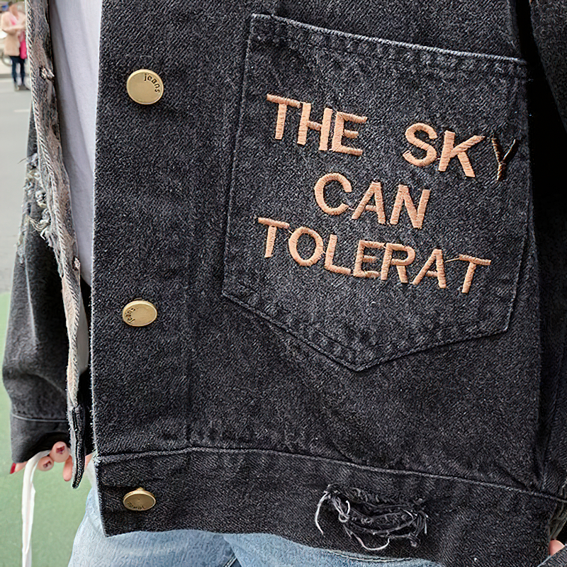 Casual black denim jacket with embroidered phrase 'THE SKY CAN TOLERAT' on pocket for stylish everyday wear.