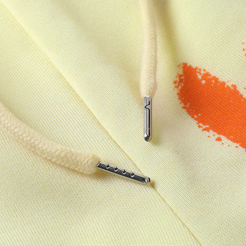 Close-up of yellow fleece hoodie drawstrings with metallic tips and vibrant orange design, showcasing casual style.