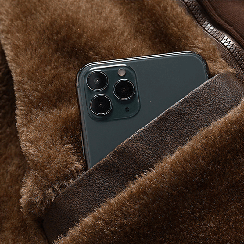 Close-up of a smartphone tucked into the pocket of a warm brown fleece-lined faux leather jacket.