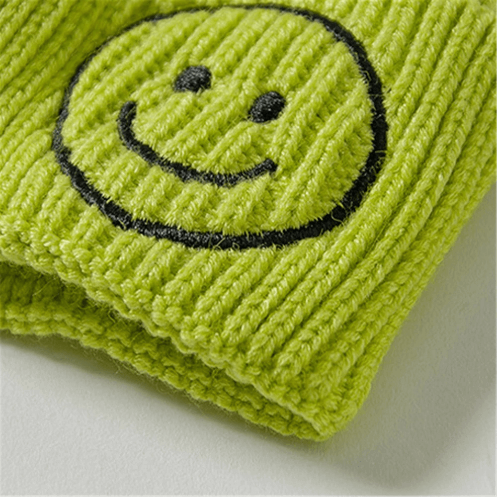 Close-up of a green knitted hat featuring a cheerful smiley face print, perfect for casual wear.