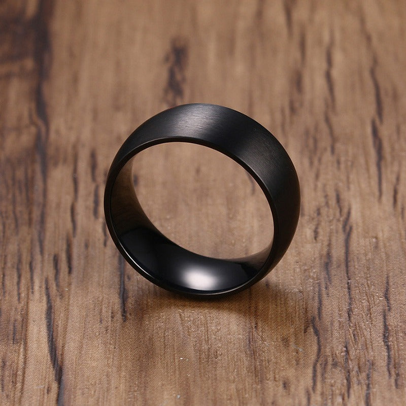 Classic black stainless steel ring with matte finish on a wooden surface, perfect for alternative engagement or stylish accessory.