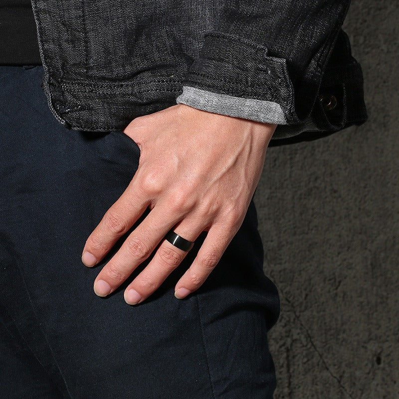 Hand wearing a classic black stainless steel engagement ring with a matte finish, showcasing a trendy accessory.