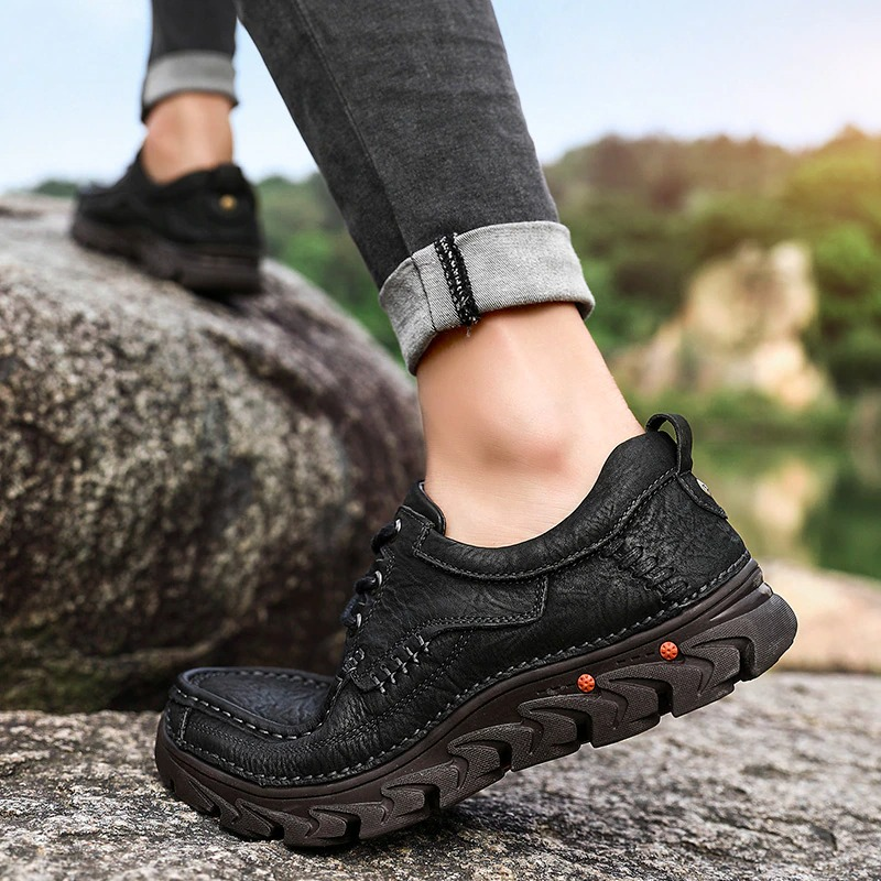 Close-up of a man's black leather lace-up shoes on rocky terrain, showcasing a classic design for alternative style.