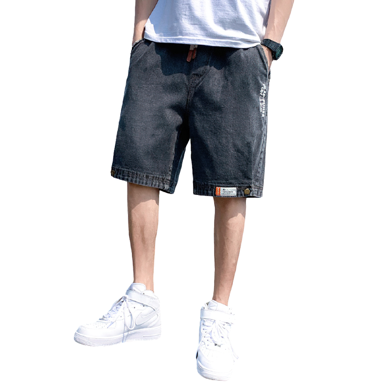 Men's cool loose denim shorts in black, styled with white sneakers for a trendy summer look.