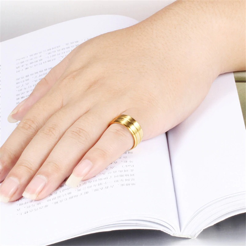 Stylish gold stainless steel unisex ring on a hand resting on an open book, perfect for any outfit.