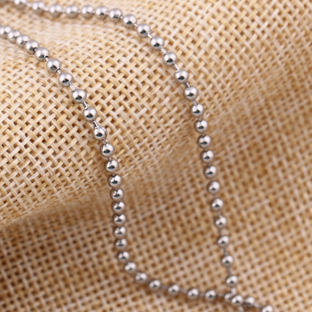 Close-up of a cool stainless steel necklace with shiny beads on a textured fabric background.