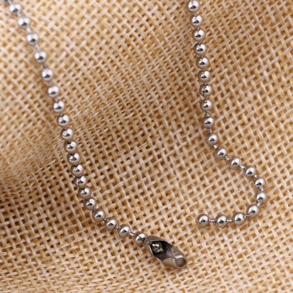 Close-up of a stainless steel necklace chain with a ball design on a textured fabric background.